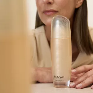 Close up of person resting their hands on a light beige glossy surface behind bottle of Ultimate The Lotion 2